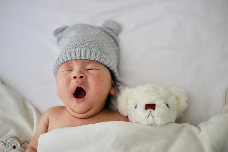 Baby yawning and hugging a teddy bear