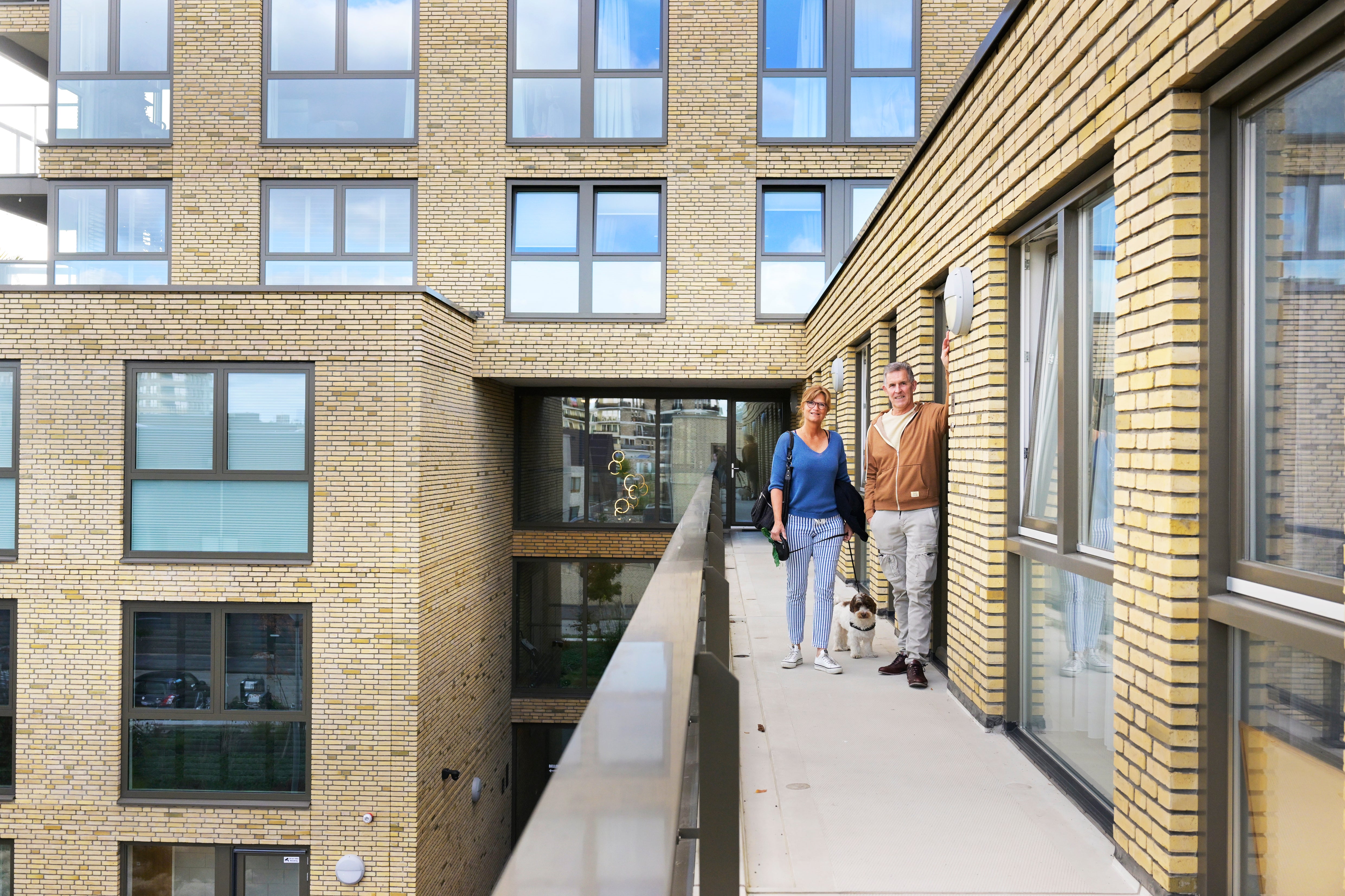Man en vrouw staan met hond bij appartementencomplex.