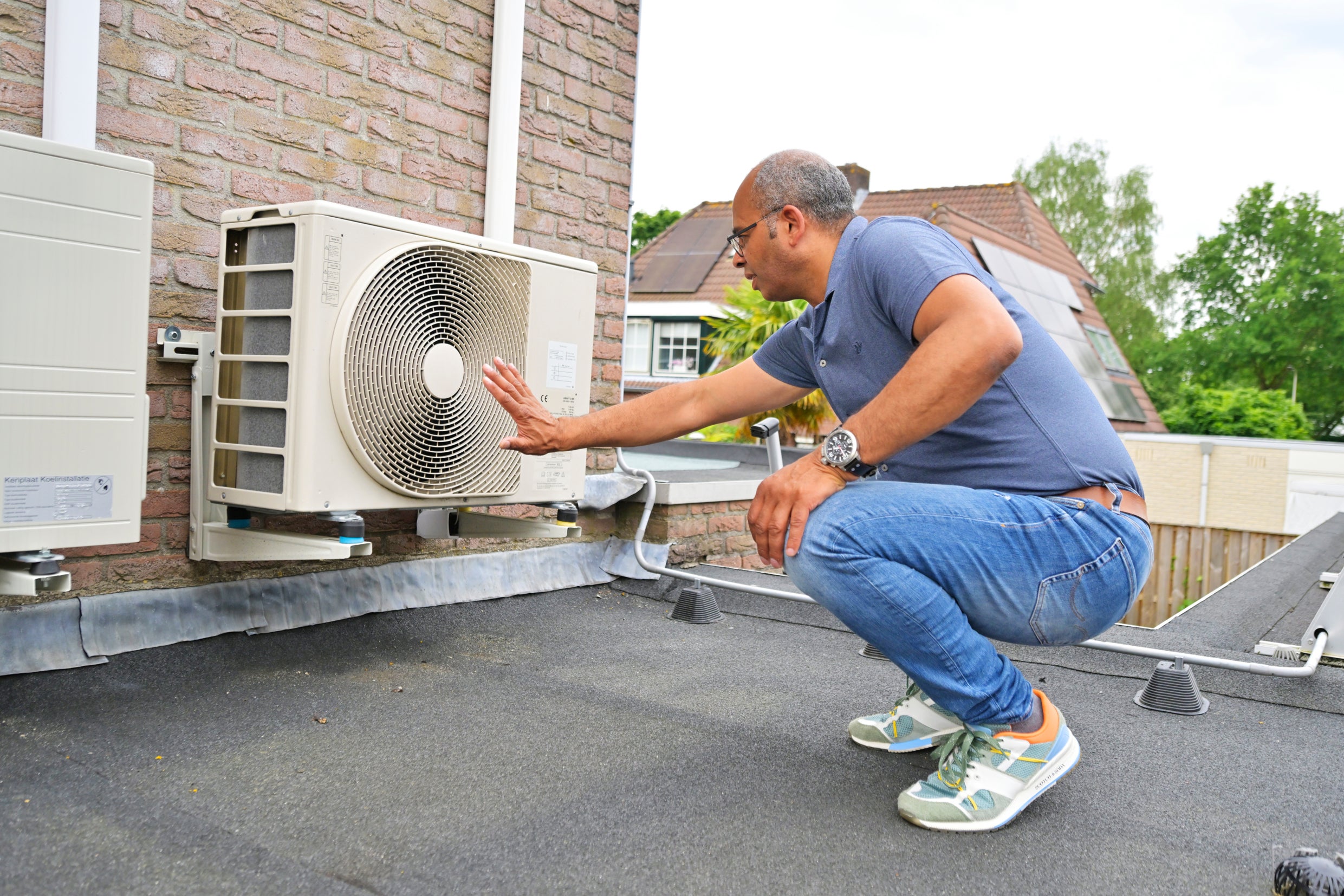 Man bekijkt buitenunit van zijn warmtepomp.