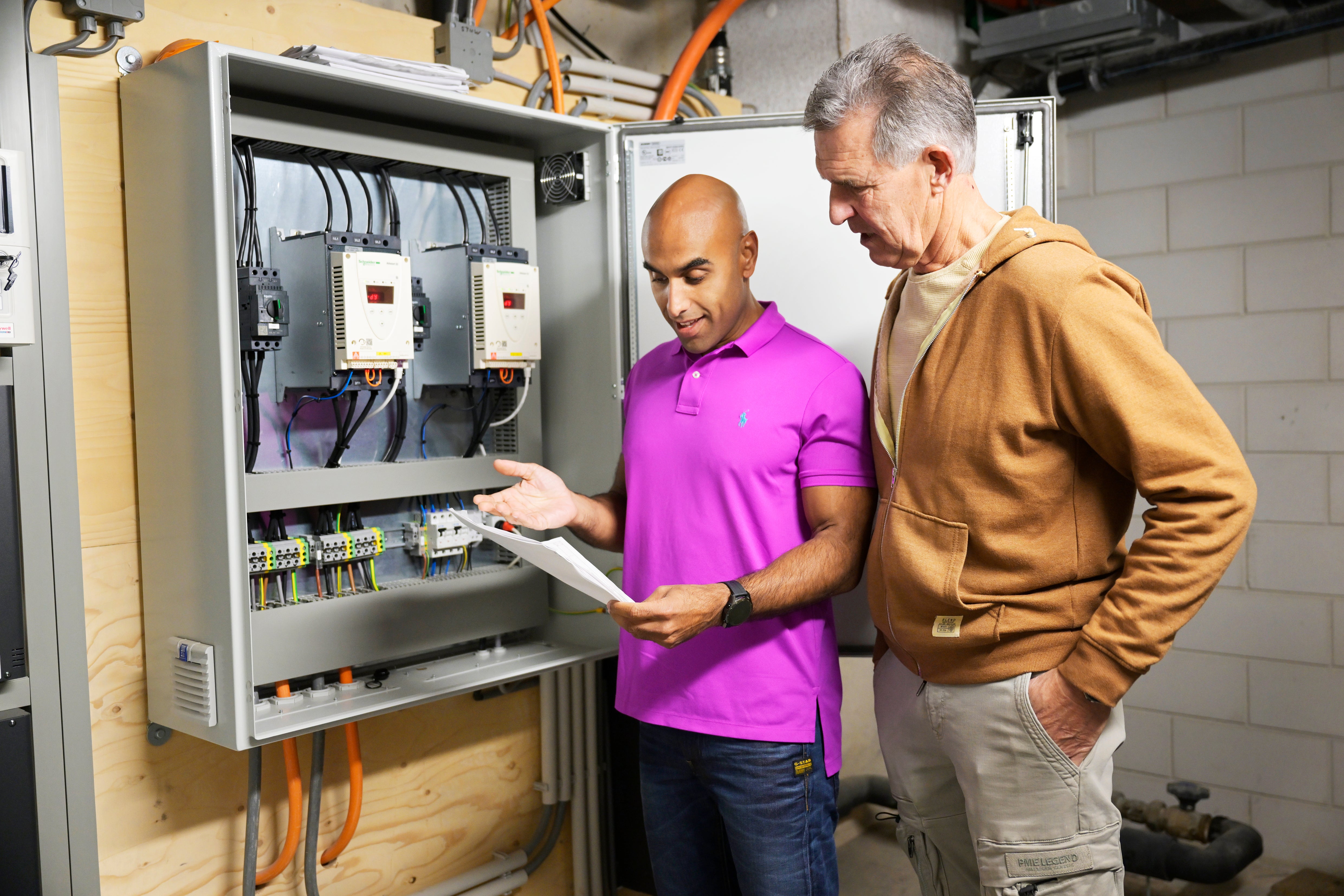 twee mannen bekijken papierwerk bij de gezamenlijke meterkast