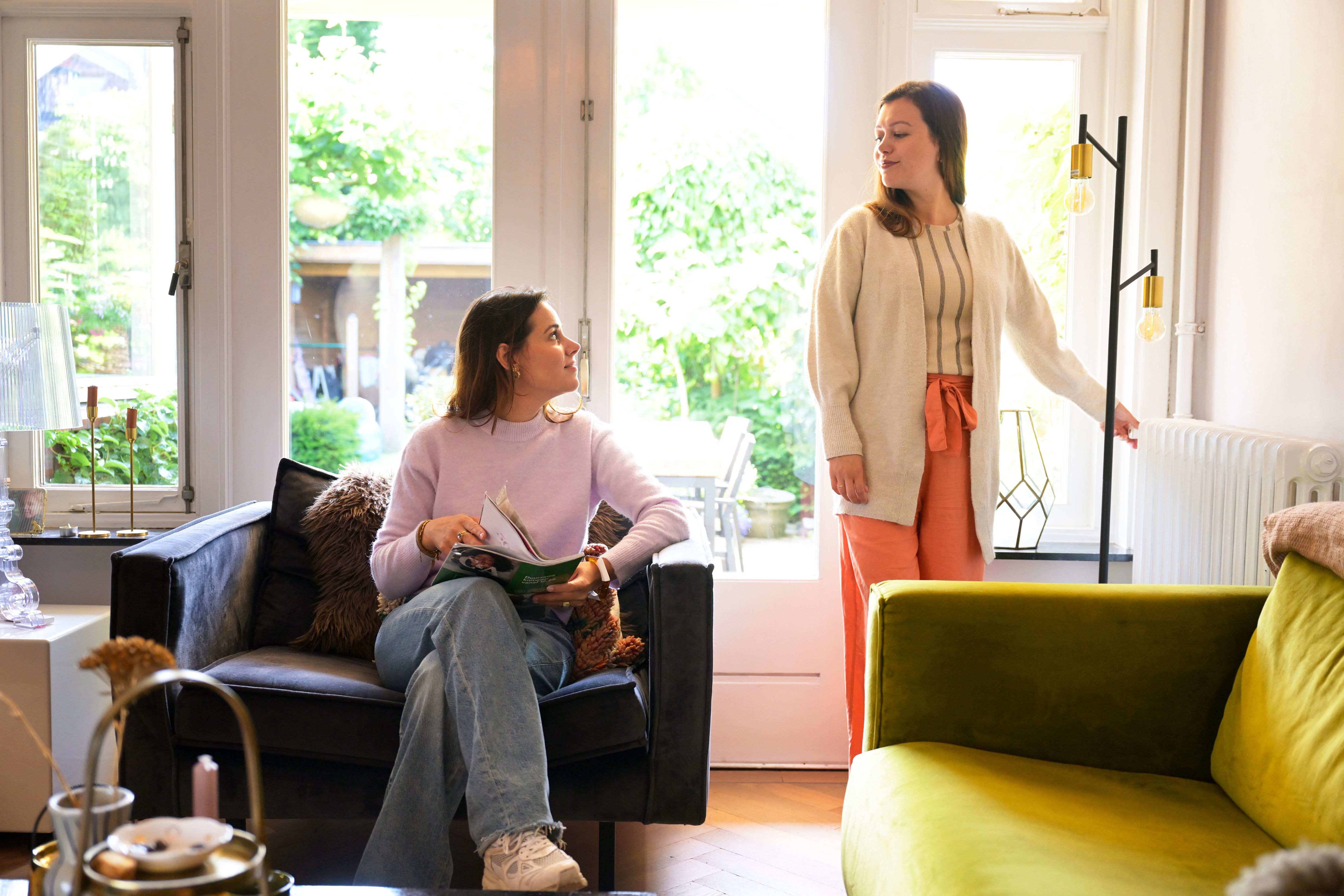 vrouw lees op de bank en andere vrouw draait aan radiatorkop