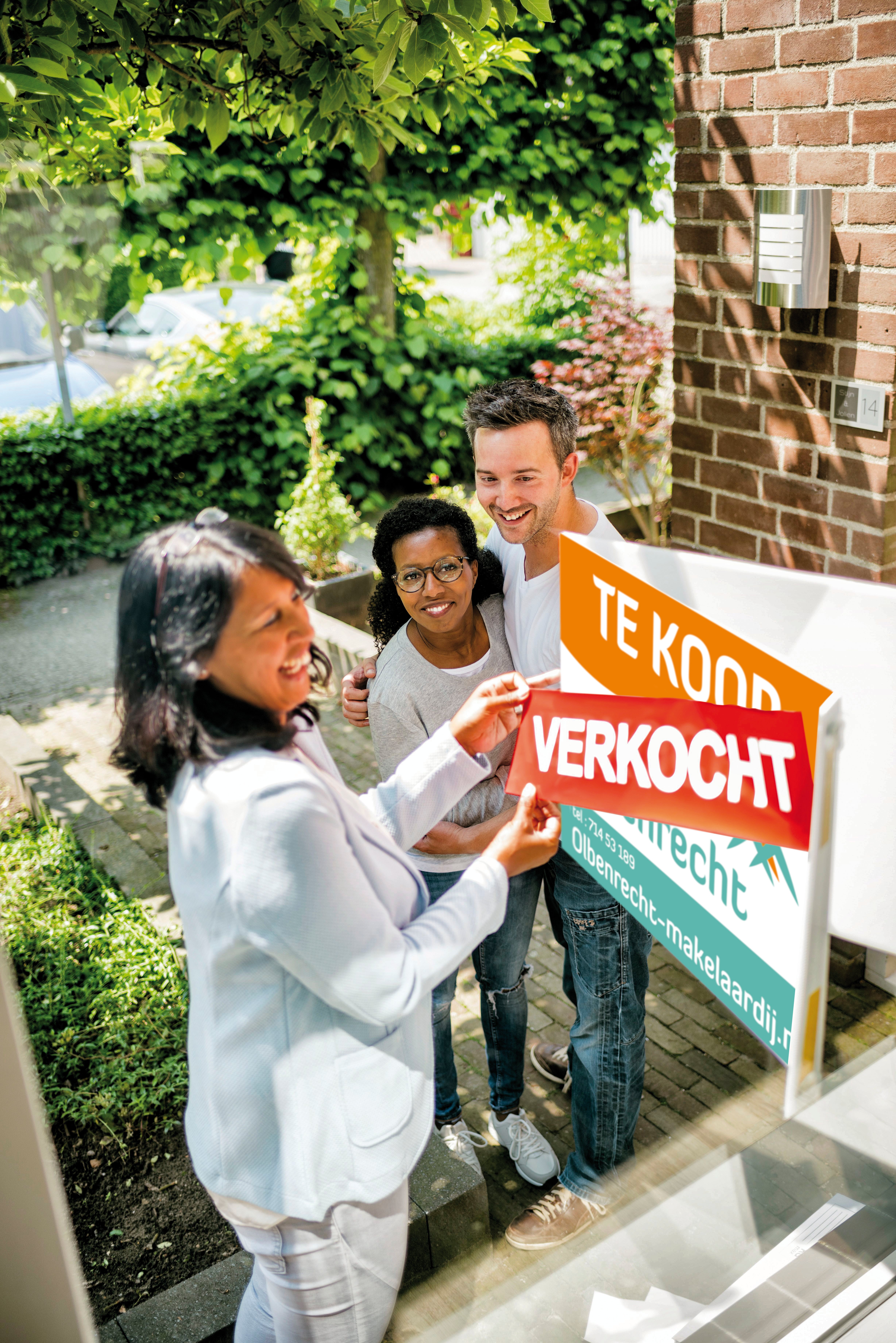 blije mensen staan bij een 'verkocht' bord
