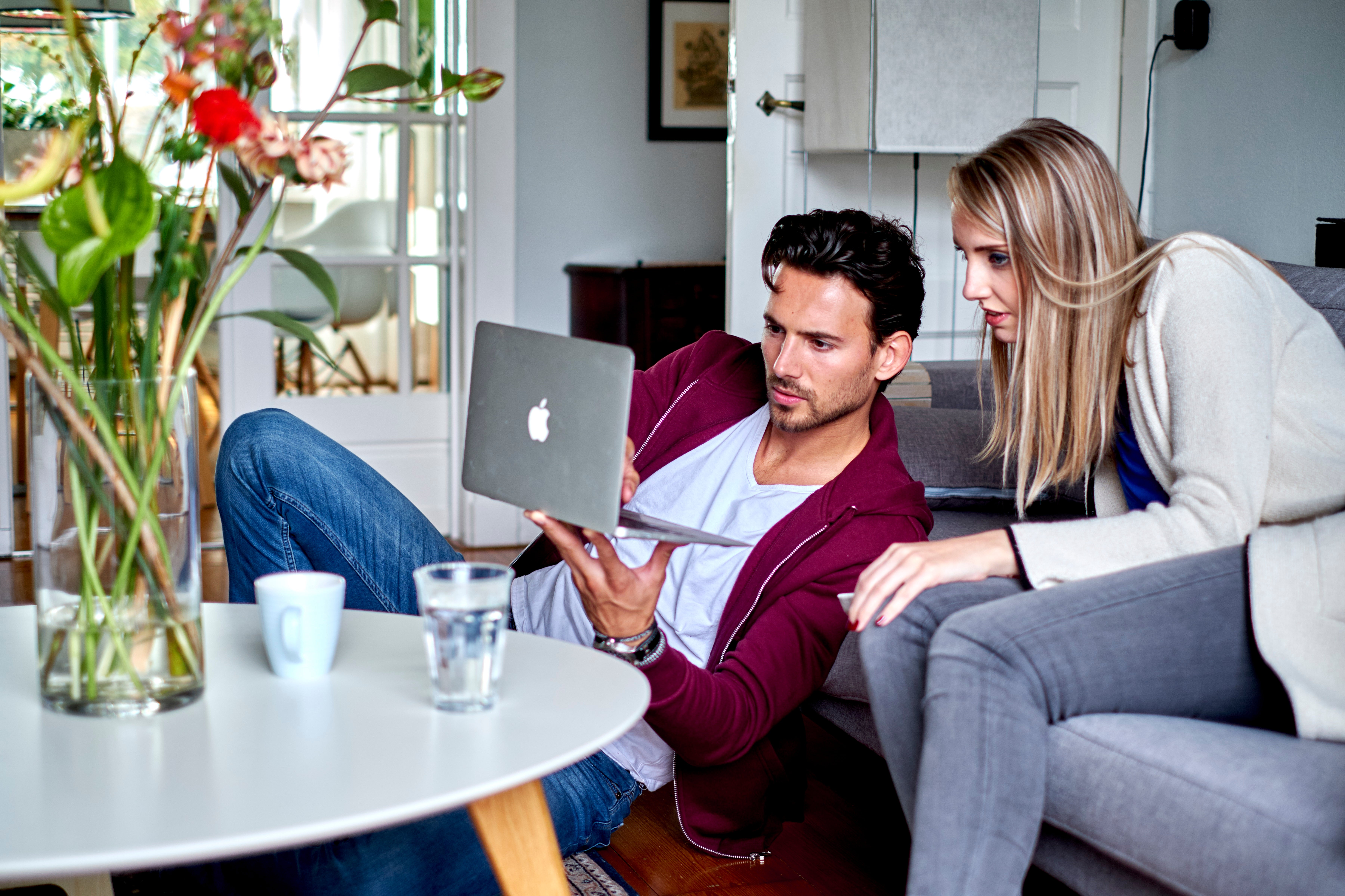 man op grond laat iets zien op laptop aan vrouw op bank