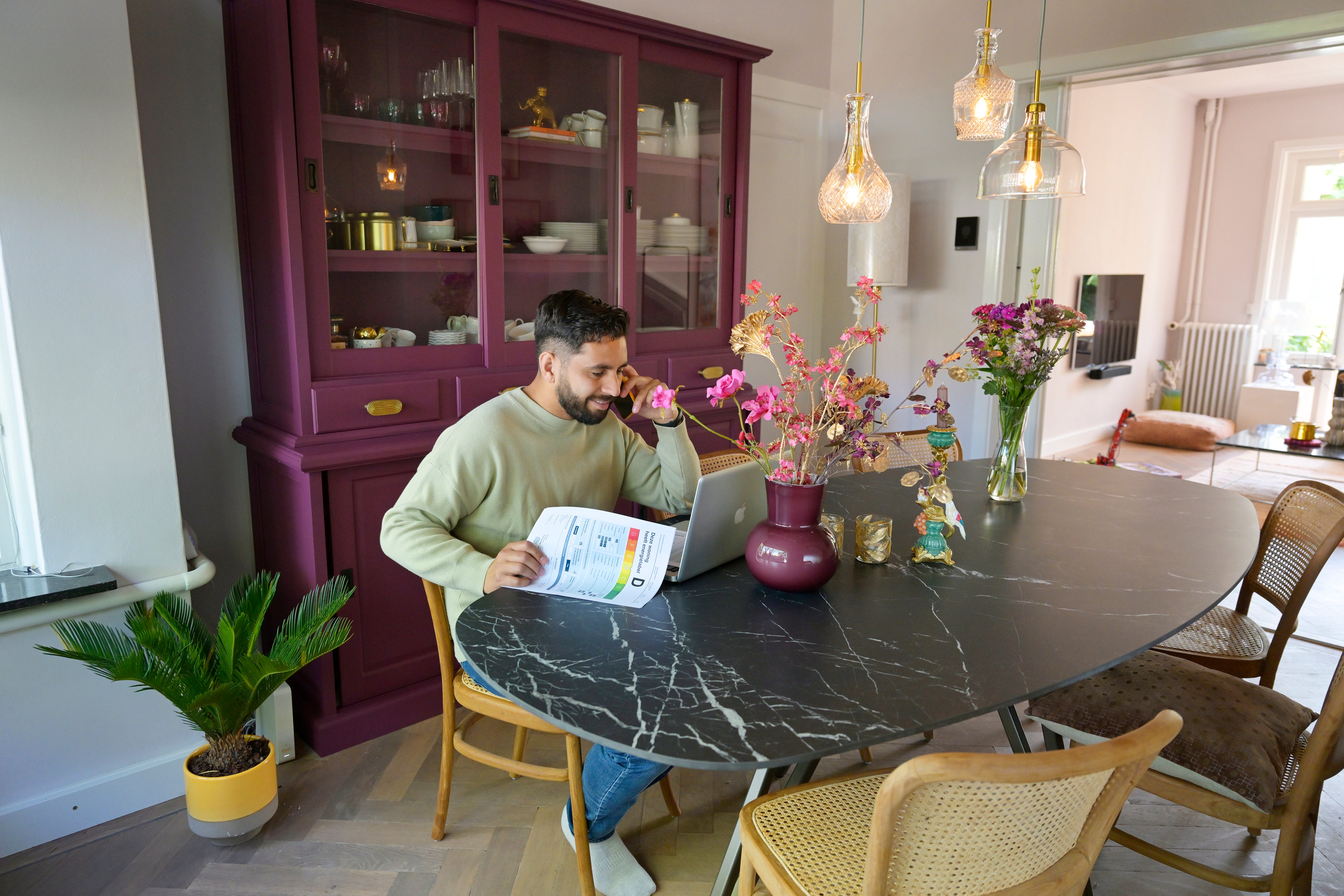 Man zit aan tafel en is aan het bellen. Hij heeft een papier in zijn hand met daarop het energielabel.