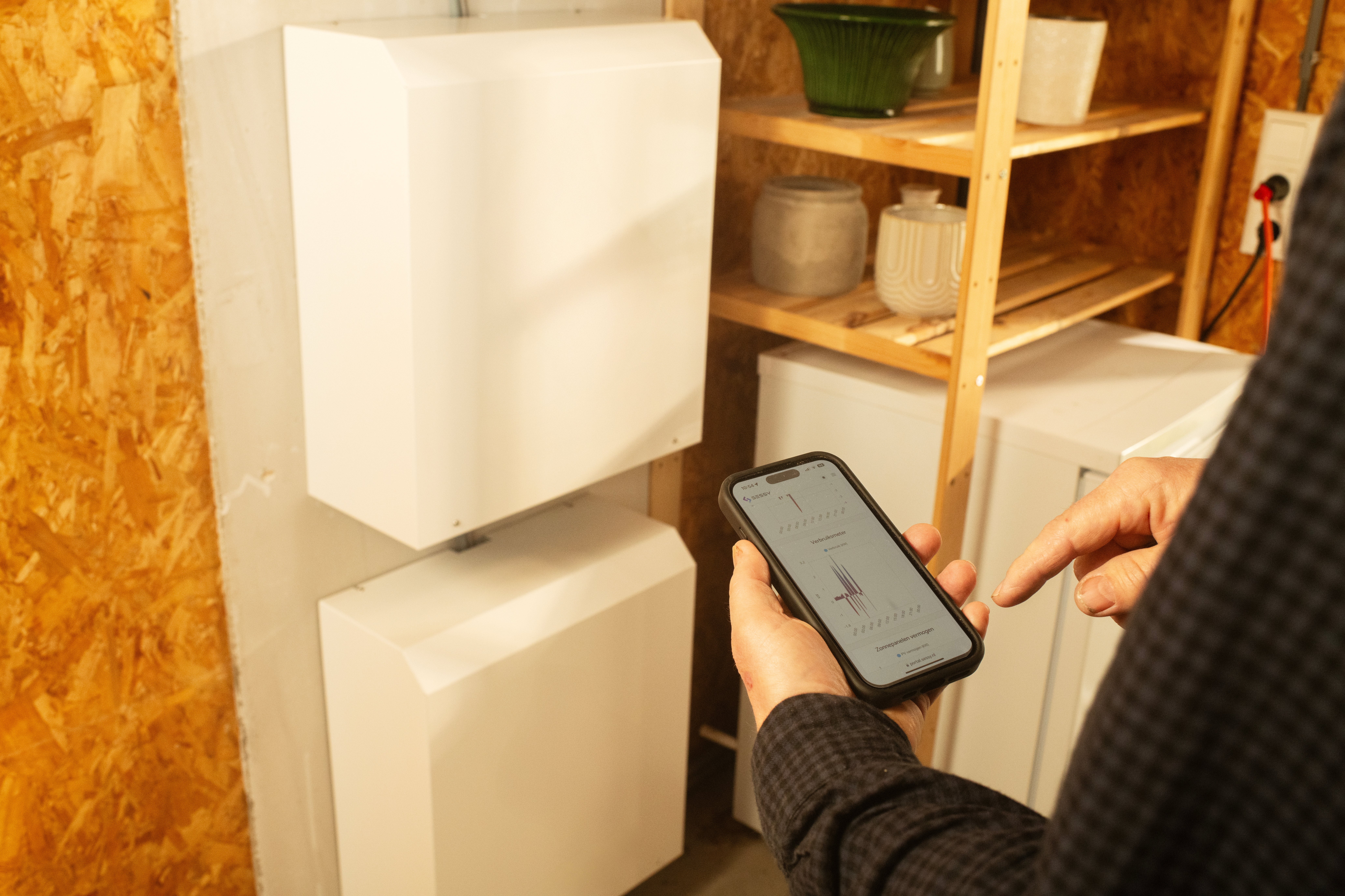 man staat bij thuisbatterij en bekijkt app 