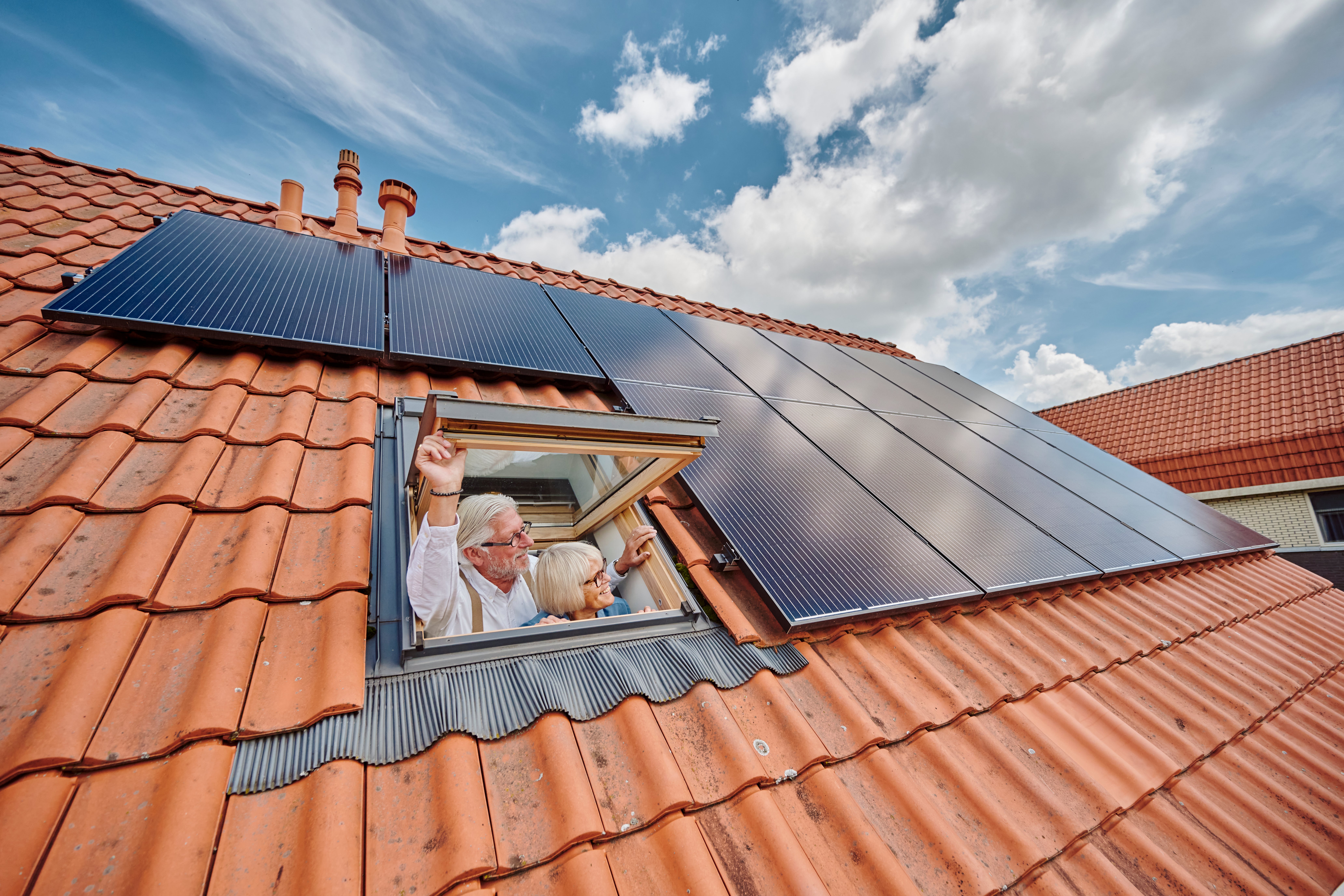 man en vrouw kijken uit dakraam naast zonnepanelen