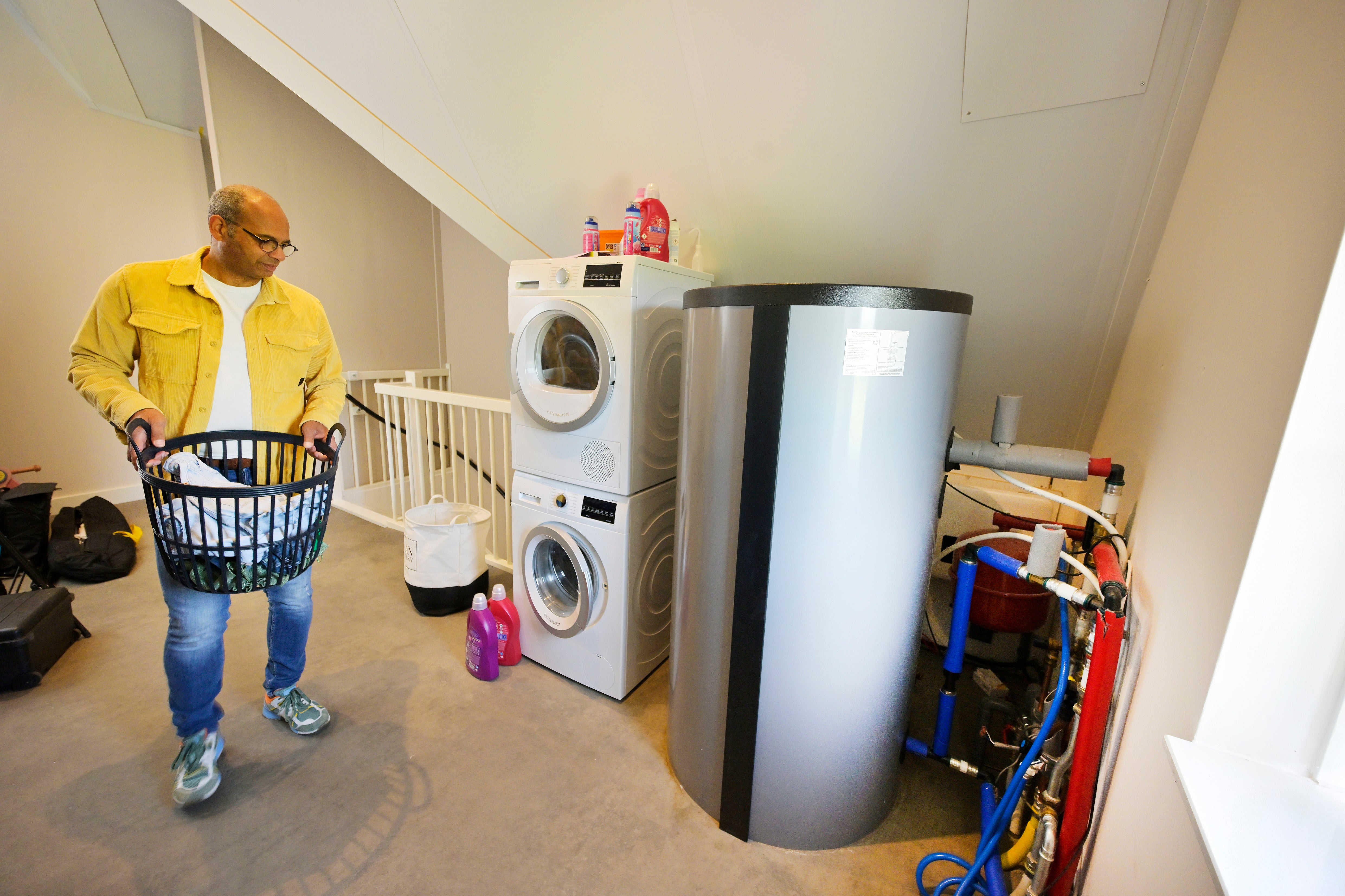 Man met wasmand loopt langs boilervat van all-electric warmtepomp. 