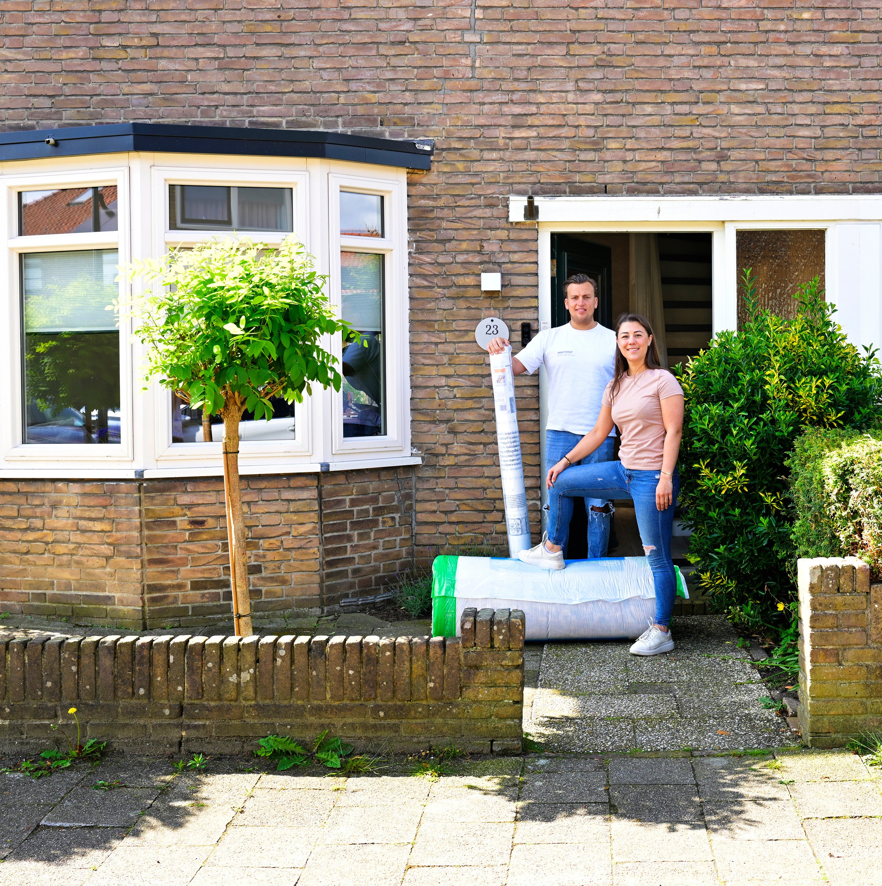 Man en vrouw staan buiten voor hun voordeur en houden isolatiemateriaal vast.