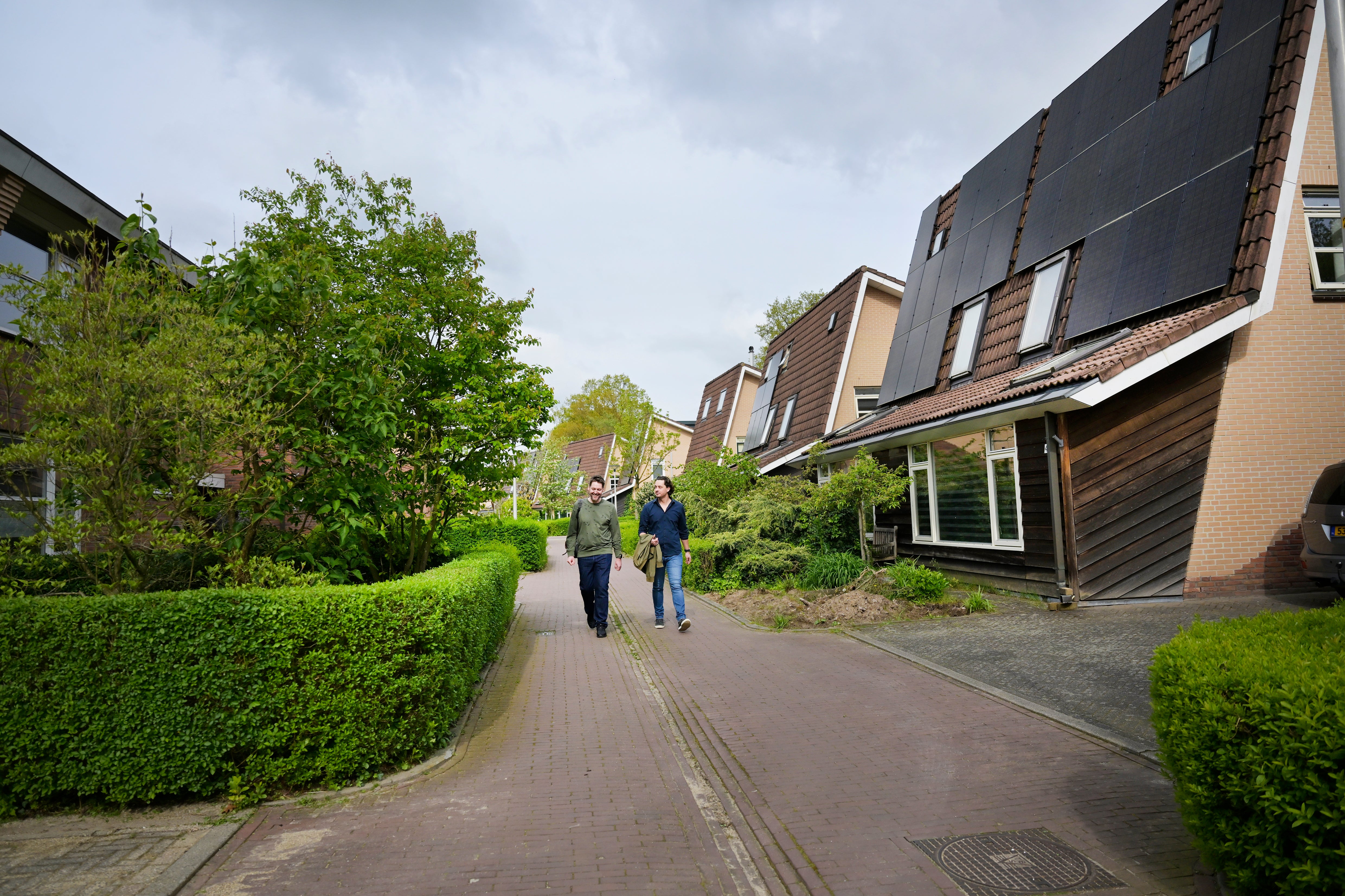 twee mannen lopen langs woning met zonnepanelen