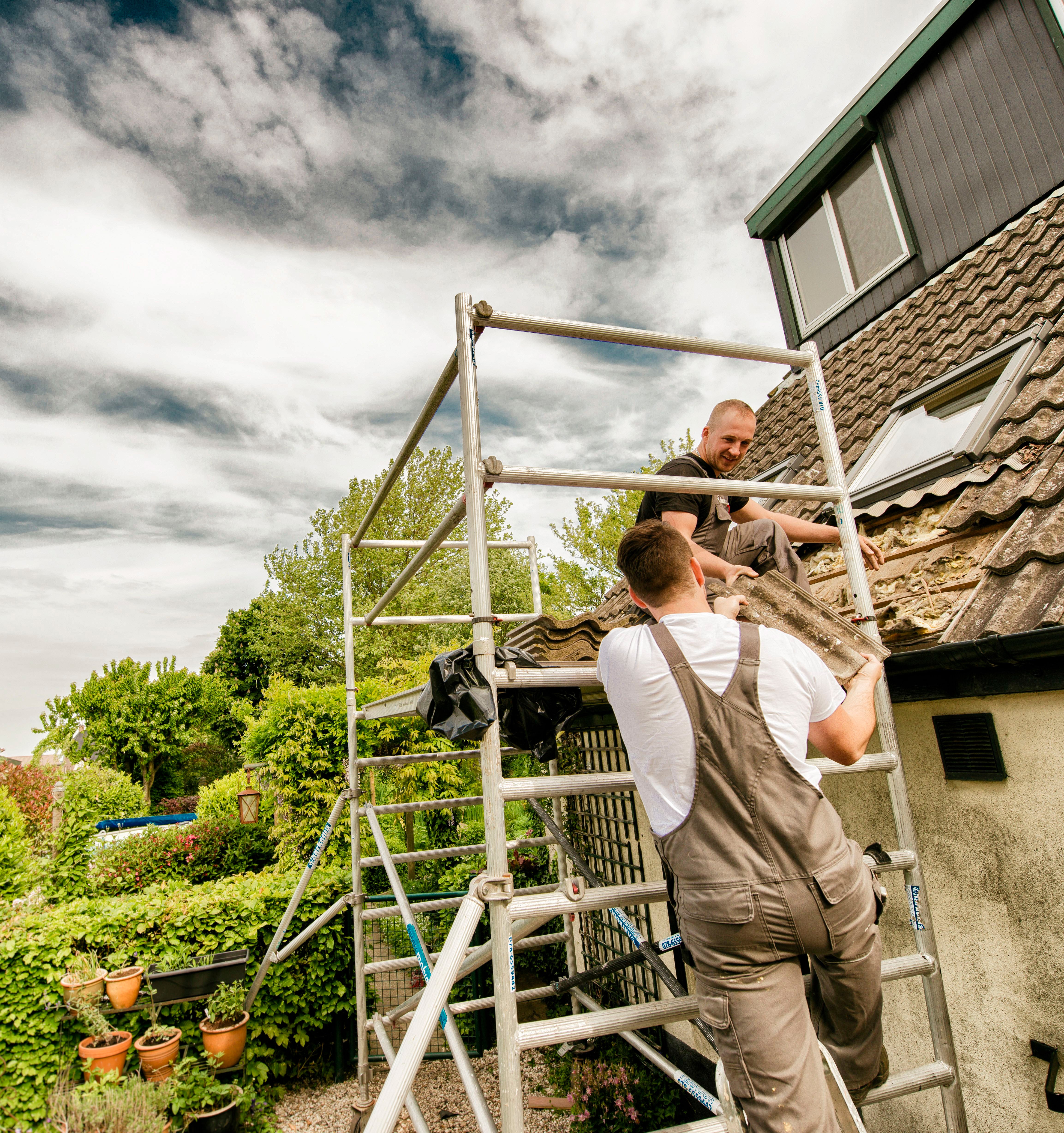 Twee mannen staan buiten met een stijger en vervangen samen dakpannen.