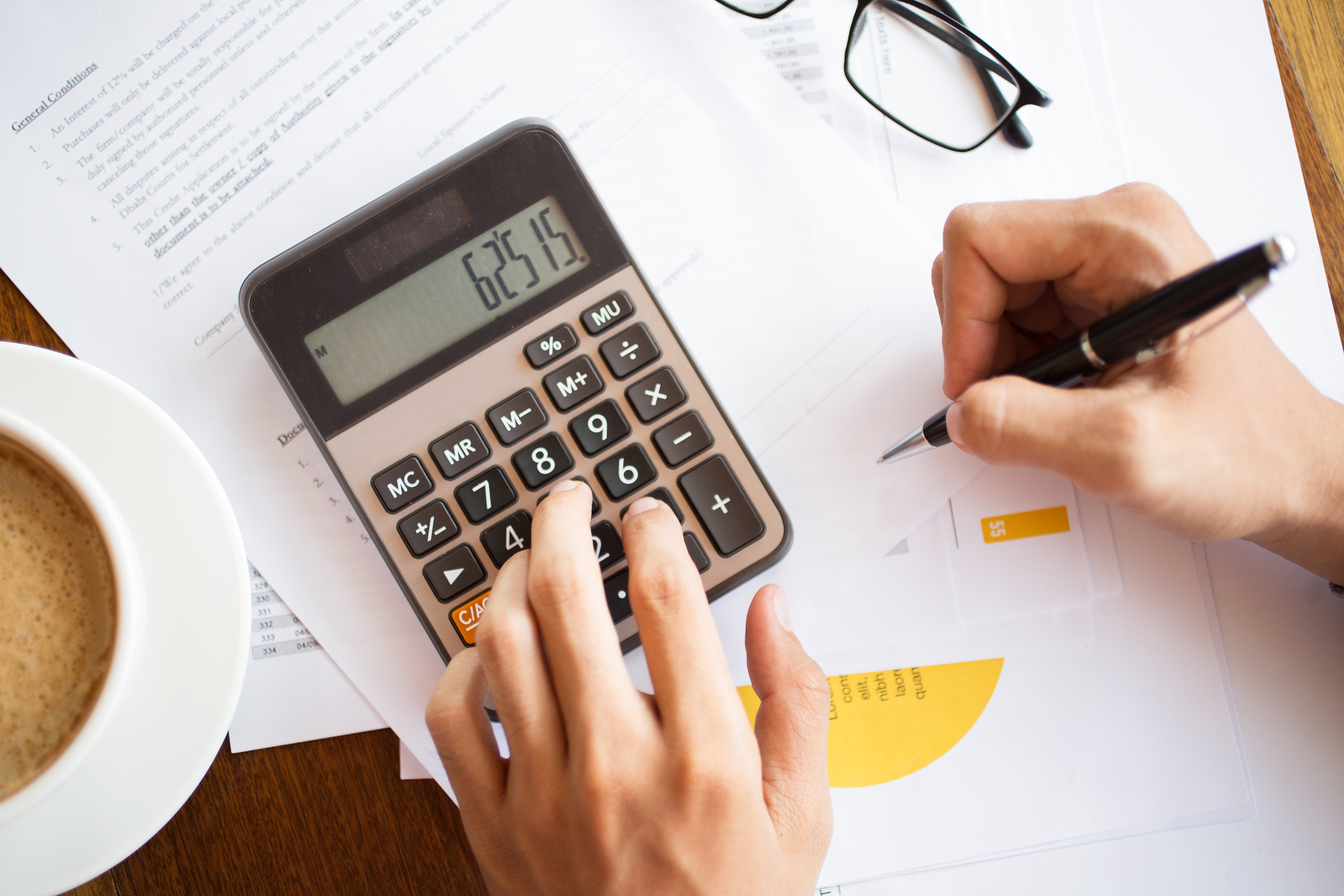 Papieren, een rekenmachine en een hand die een pen vasthoudt.