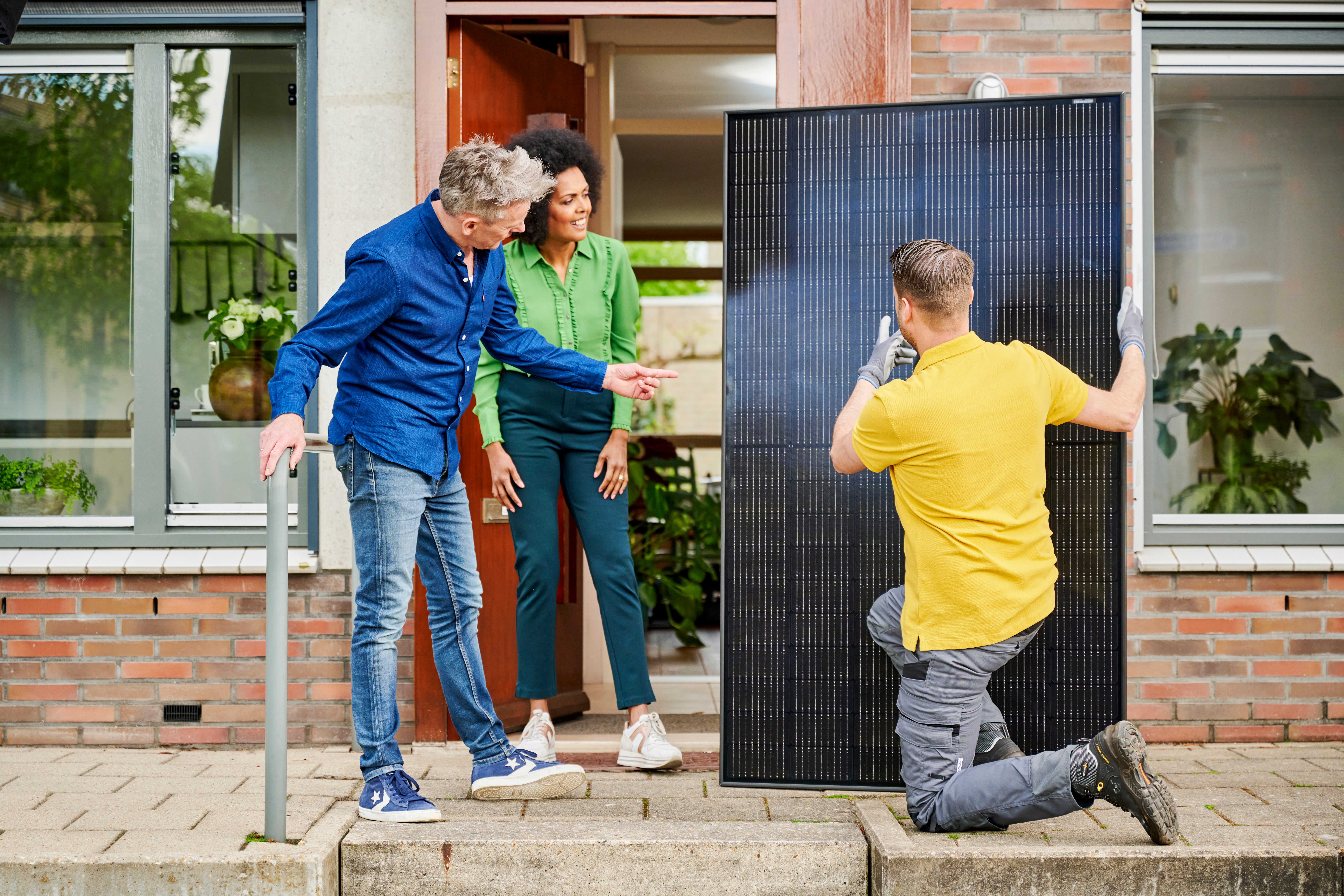 man geeft uitleg aan stel over zonnepaneel bij voordeur