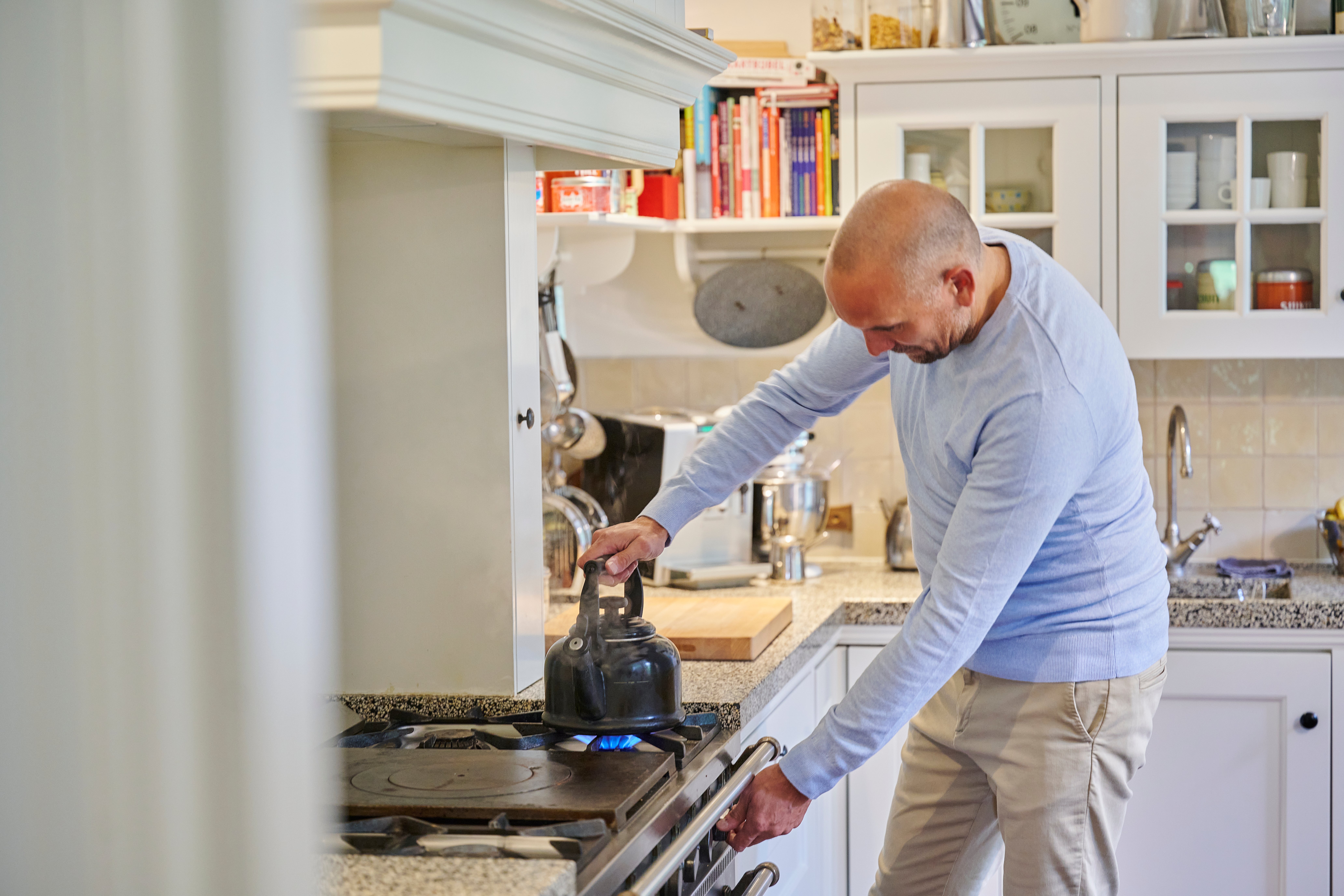 man bedient gasfornuis met fluitketel erop