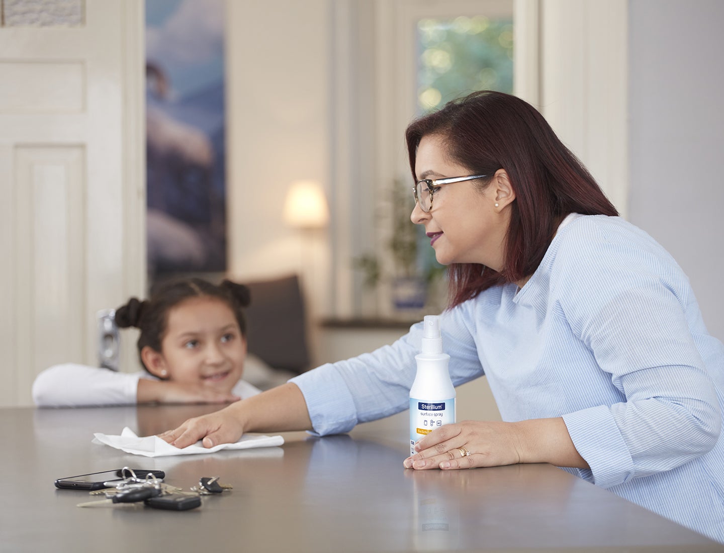 Frau desinfiziert den Tisch mit Sterillium® Surface Spray und Kind schaut zu