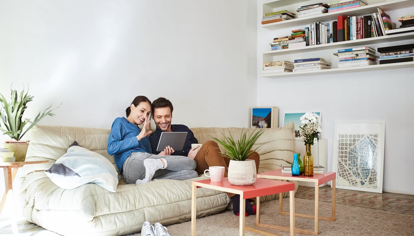 Un jeune couple est assis sur le canapé et regarde un appareil mobile.