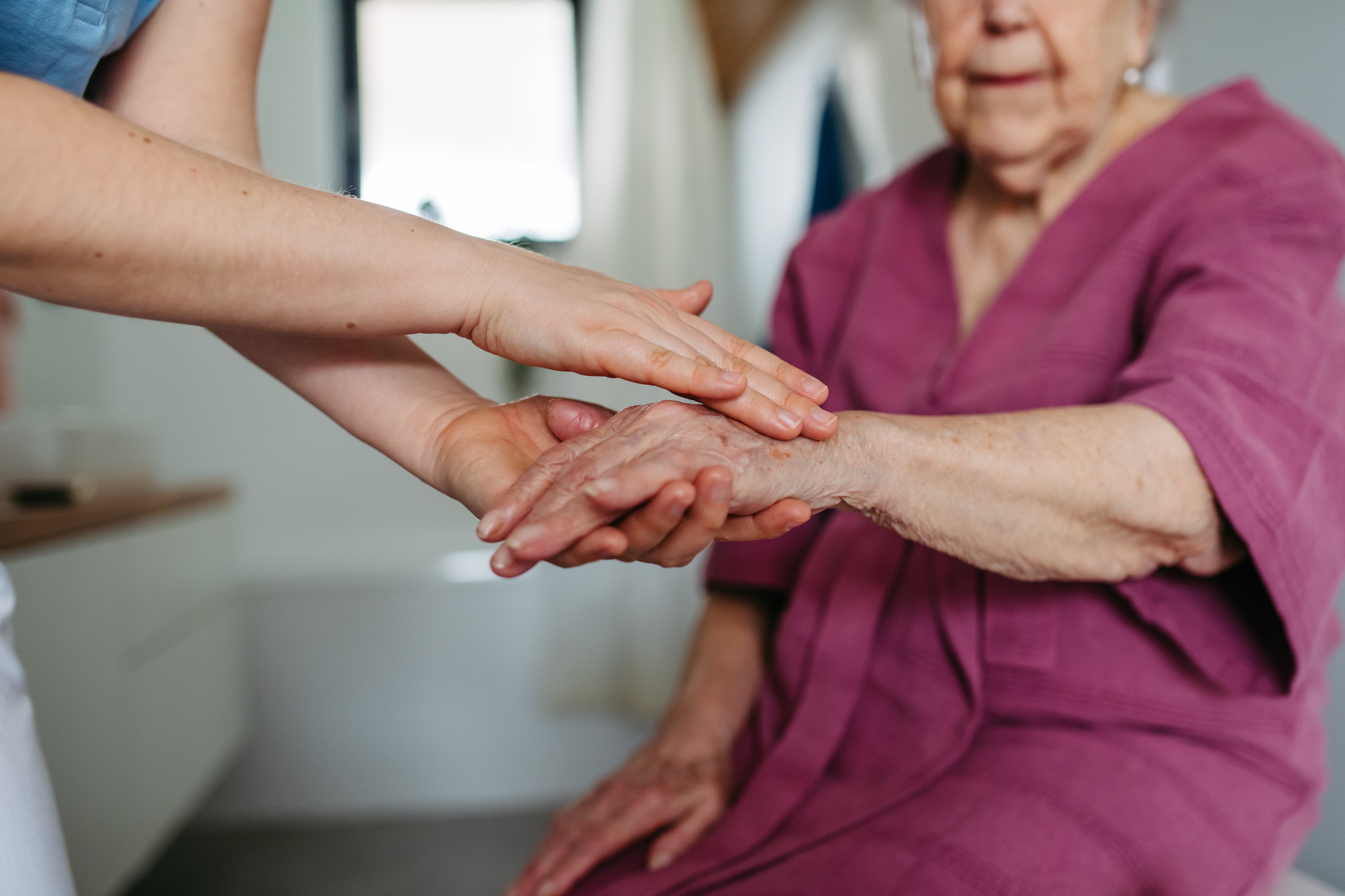 Pflegekraft hält die Hand einer älteren Dame