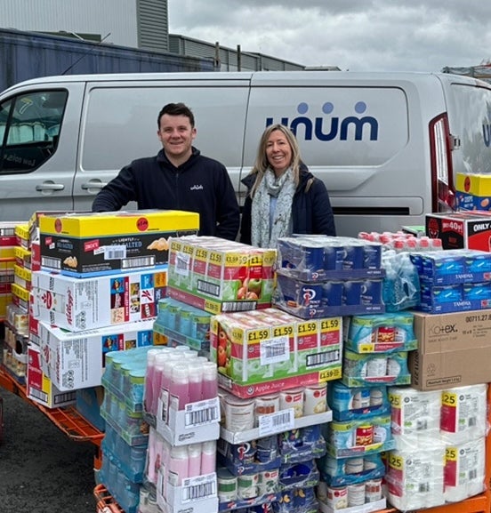 A man and woman standing next to a truck with a stack of boxes of beverages