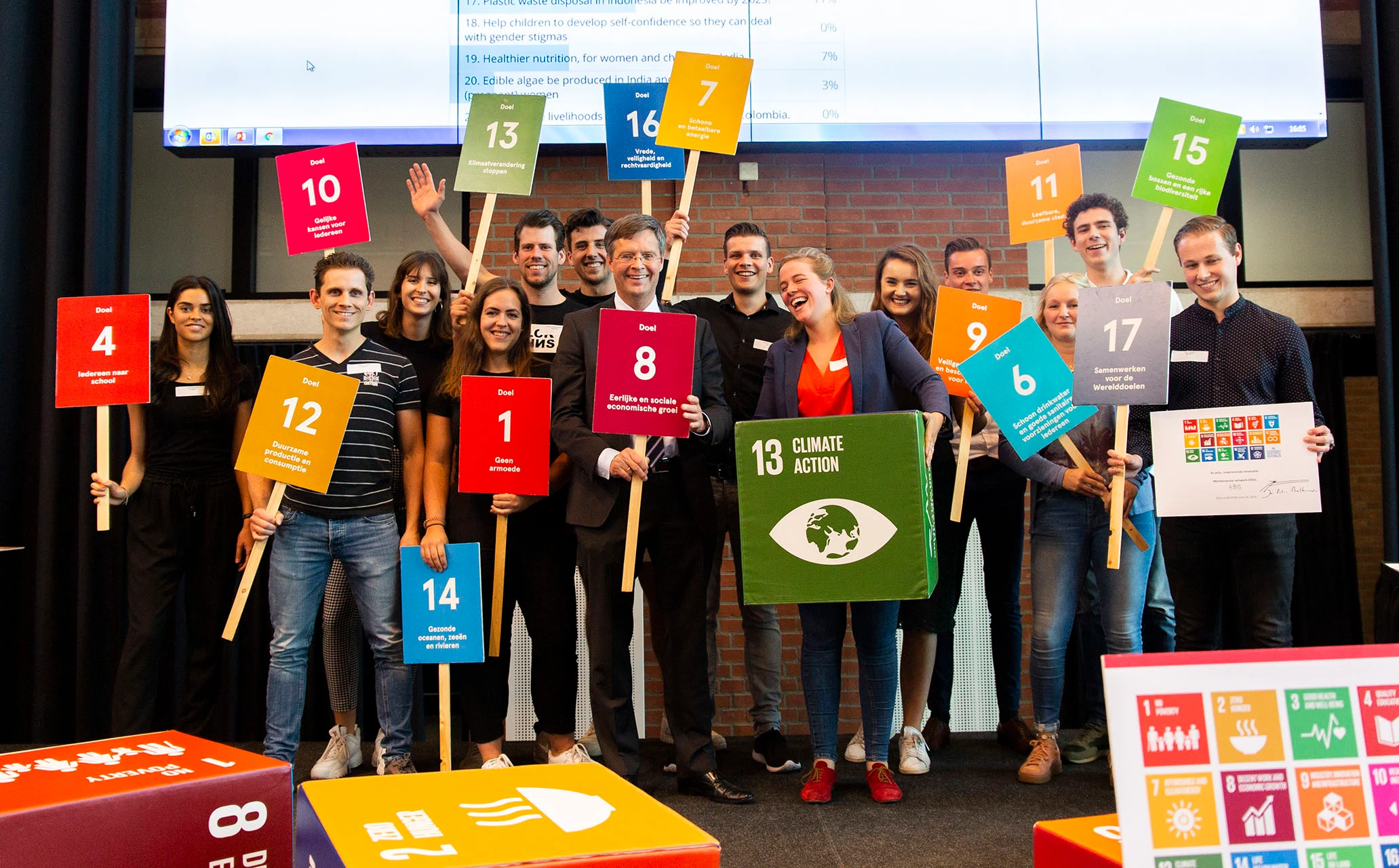 Groep studenten op een podium samen met Peter-Jan Balkenende. Waarbij ze borden vasthouden waarop alle SDG's vermeld staan