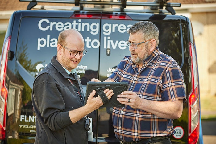 Two colleagues standing beside a branded van, looking at and using a tablet together.