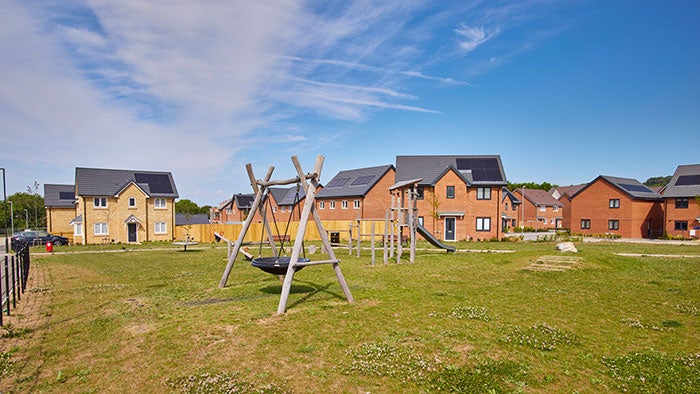 Modern family homes with rooftop solar panels surrounding a landscaped green space and children's play area, demonstrating investment in sustainable housing and community facilities.