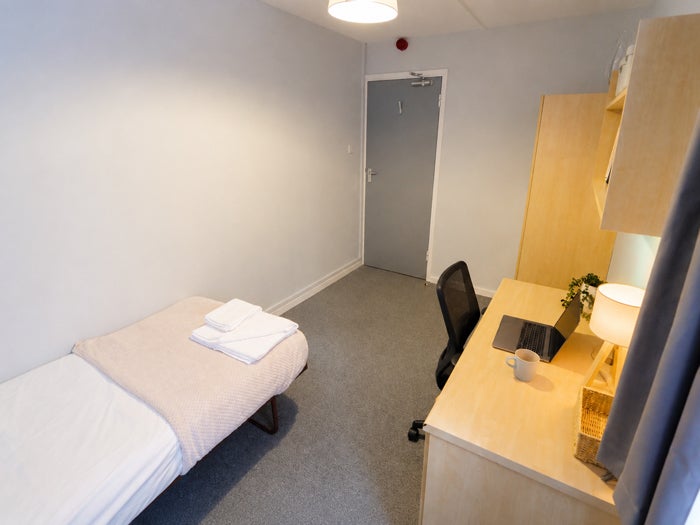 Compact single bedroom with desk, bed and storage.