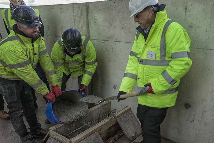 Men in high vis and hard helmets pose with spade and concrete mix