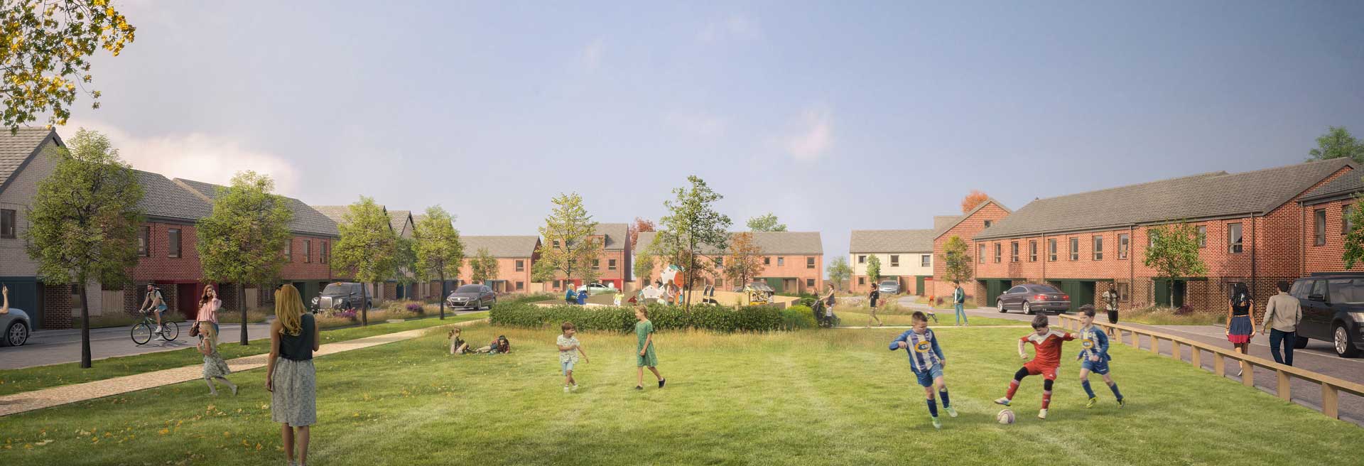 Residential development centred around a large green space, with people playing football, walking and cycling among landscaped planting, surrounded by red-brick homes and tree-lined paths.