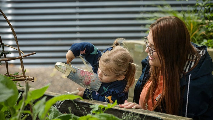 Mother supervising her daughter while she waters plants with a pretty watering can