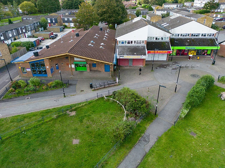 Aerial view of local shops and a pedestrian area next to a green open space in a residential neighbourhood.