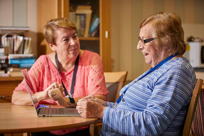 An SNG employee talking to a resident at her kitchen table. There is a laptop in front of her.