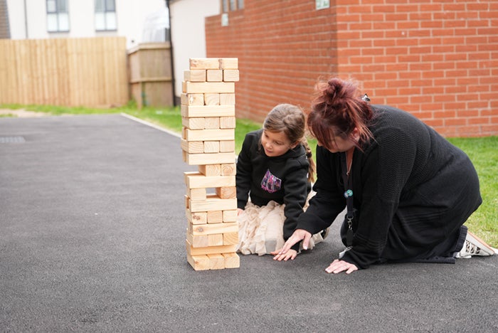 Two people kneeling on a paved area outdoors, playing a large wooden block stacking game.