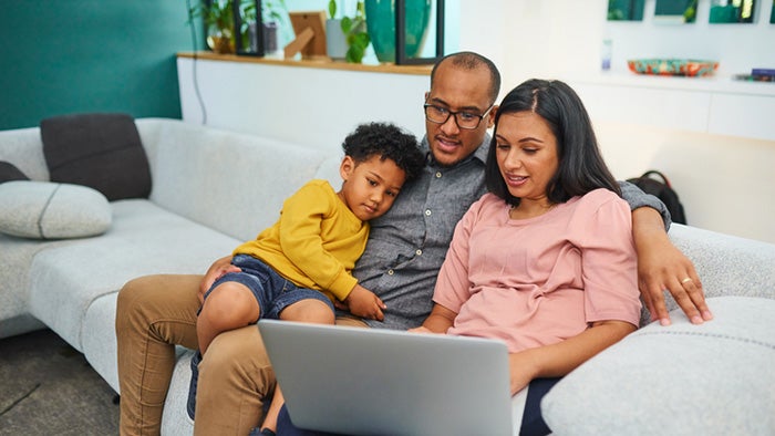 A family sitting on a sofa together looking at a laptop