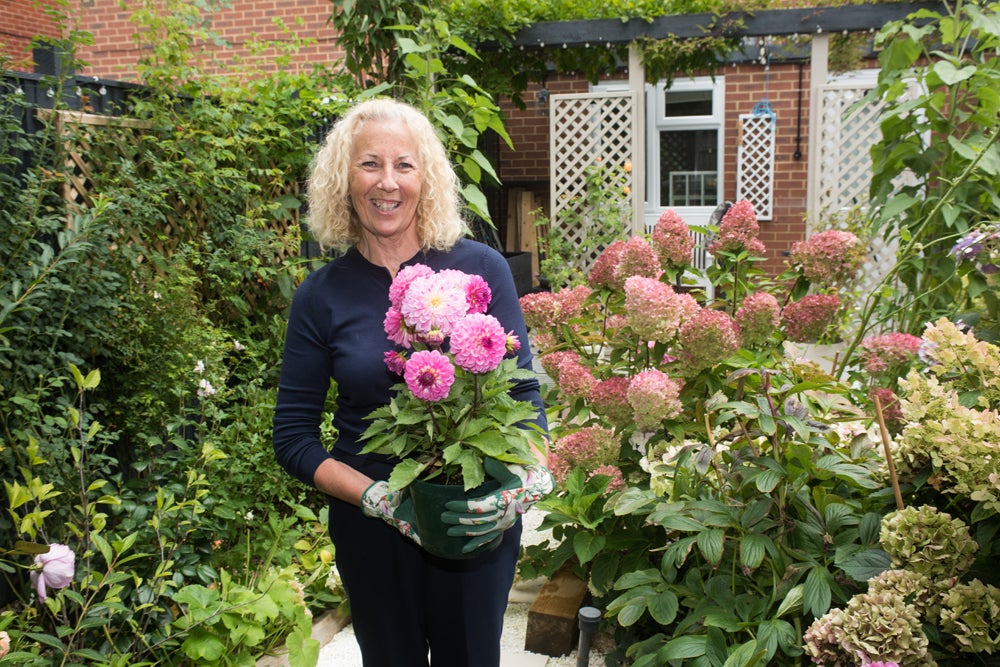Woman smiling at the camera while holding a pink plant in a vibrant garden
