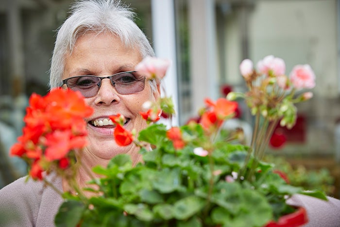 A smiling lady with a pretty red flower in front of her