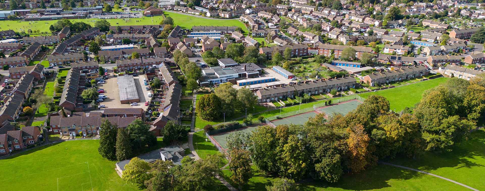 Aerial view of a residential neighbourhood with housing, green open spaces, a community building and outdoor sports courts.