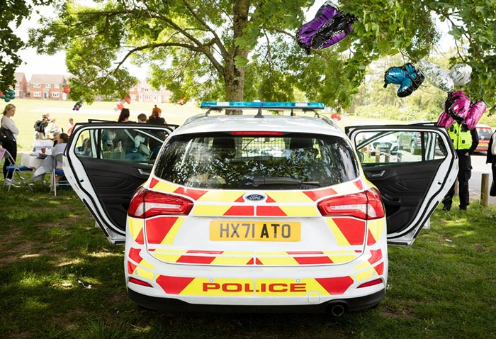 The back of a Police car parked in a wooded area with the doors open