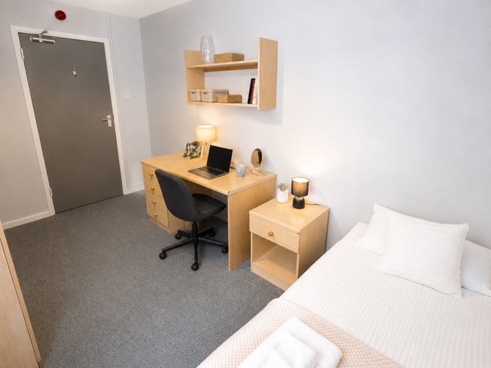 Bright single bedroom with desk, shelving and bedside storage