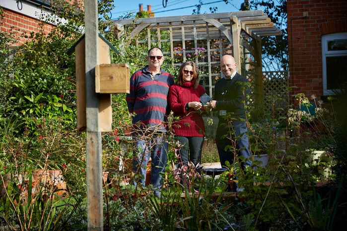 A lady and two men standing in a pretty garden on a sunny day facing the camera