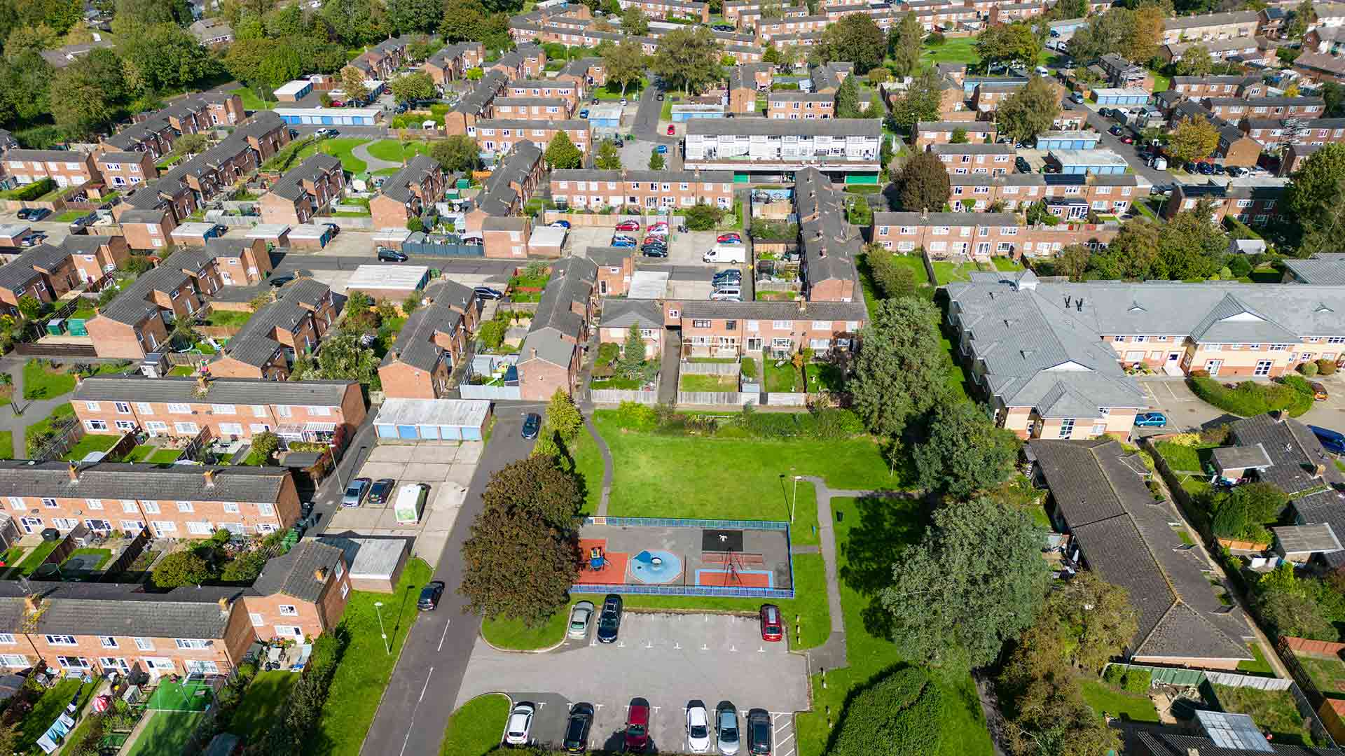 Aerial view of a residential neighbourhood with rows of brick homes, communal green space and a children's playground.