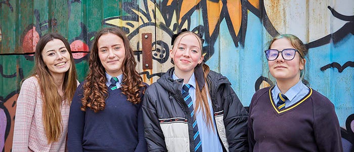 An iWill project officer with some children standing in front of graffiti. 