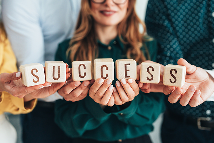 Wooden letter blocks spelling “SUCCESS” held in front of people