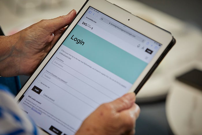 Close-up of a person holding a tablet displaying an SNG-branded login webpage, with username and password fields and a login button visible on screen.
