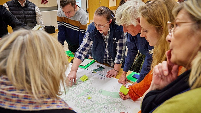 People gathered around a table reviewing a large printed plan or map, discussing and marking ideas collaboratively in a workshop setting.
