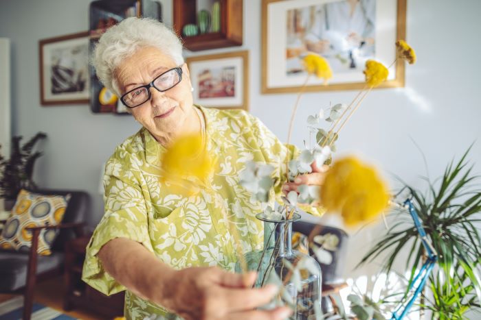 An elderly lady arranging flowers in a vase