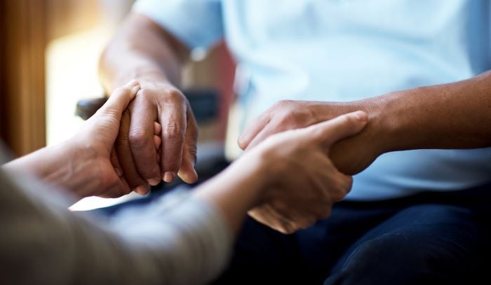 A younger person holding a vulnerable person's hands for support