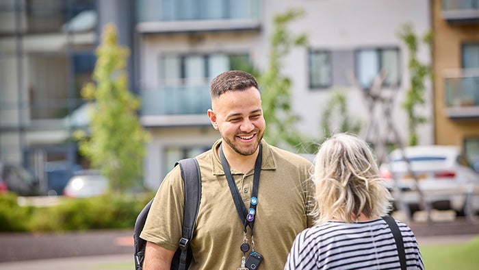 Two people talking outside modern residential buildings with greenery and landscaped surroundings