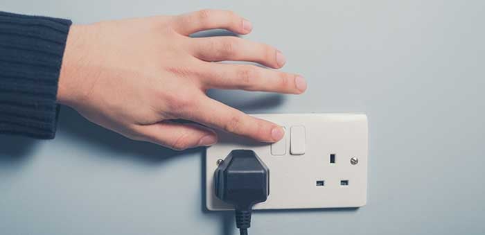 A hand is shown switching on a wall socket with a plug in it.