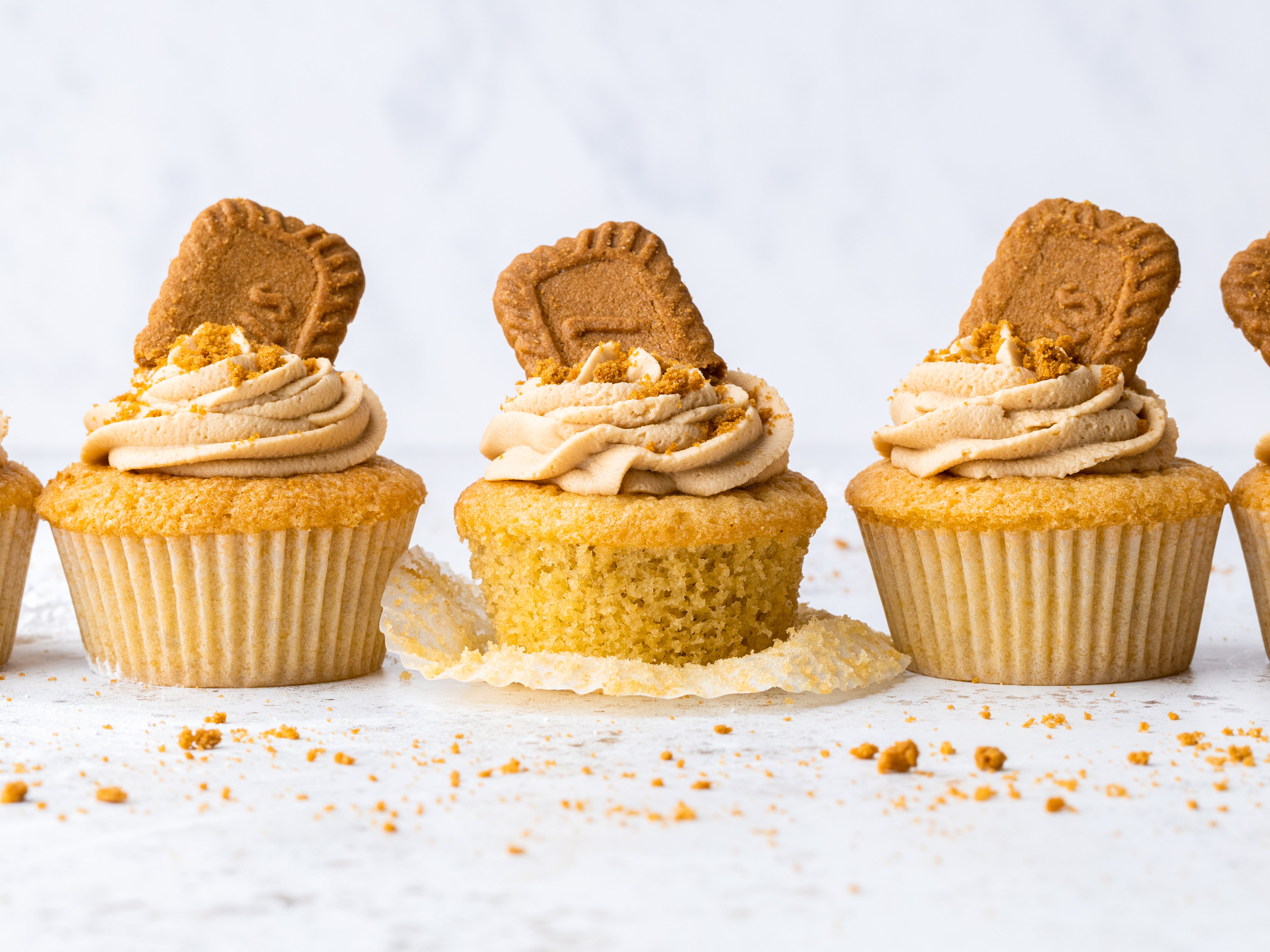 3 biscoff cupcakes in a row, one peeled and decorated with buttercream and lotus biscuit