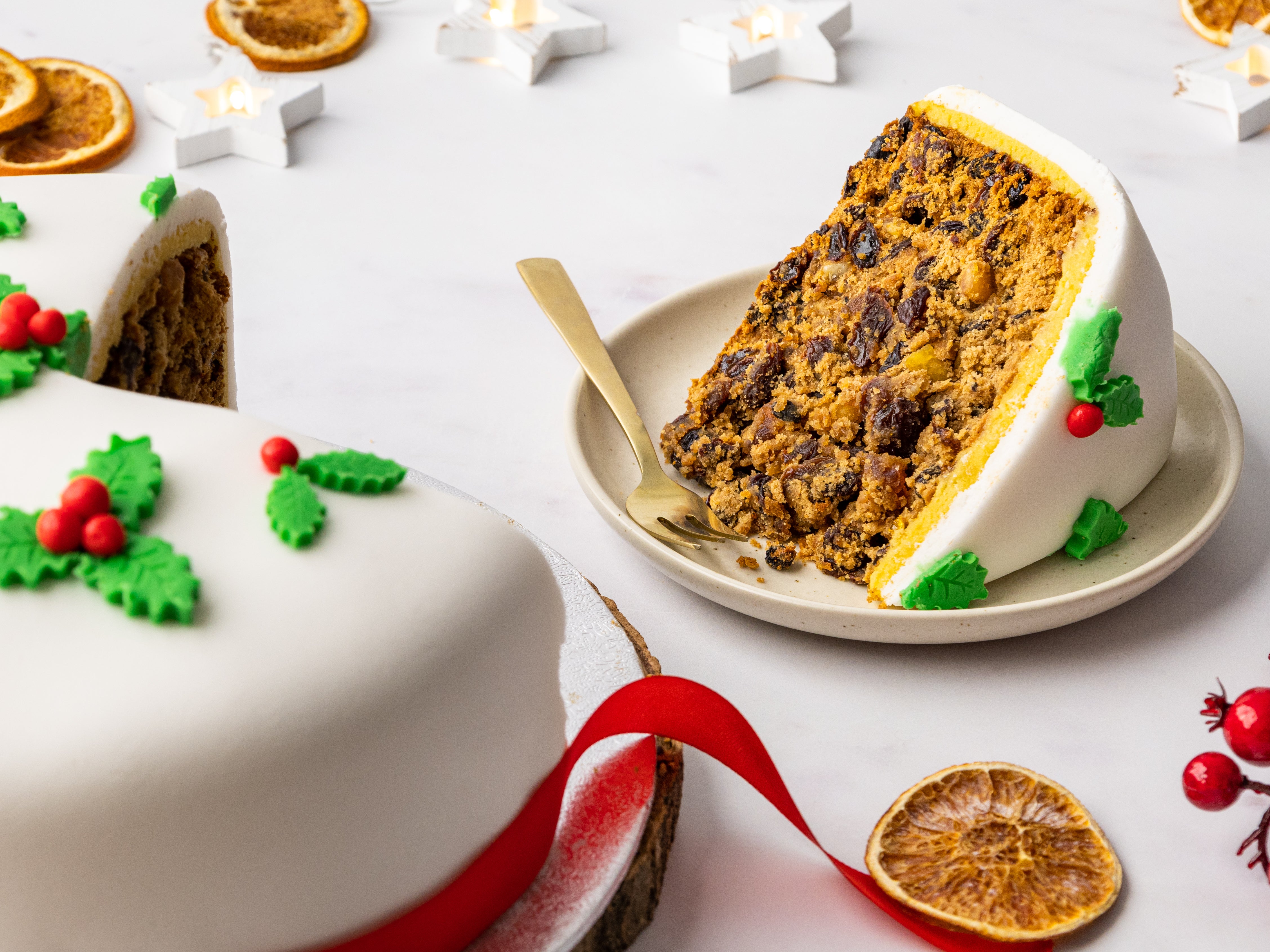 Slice of Christmas cake on a white plate decorated with fondant holly