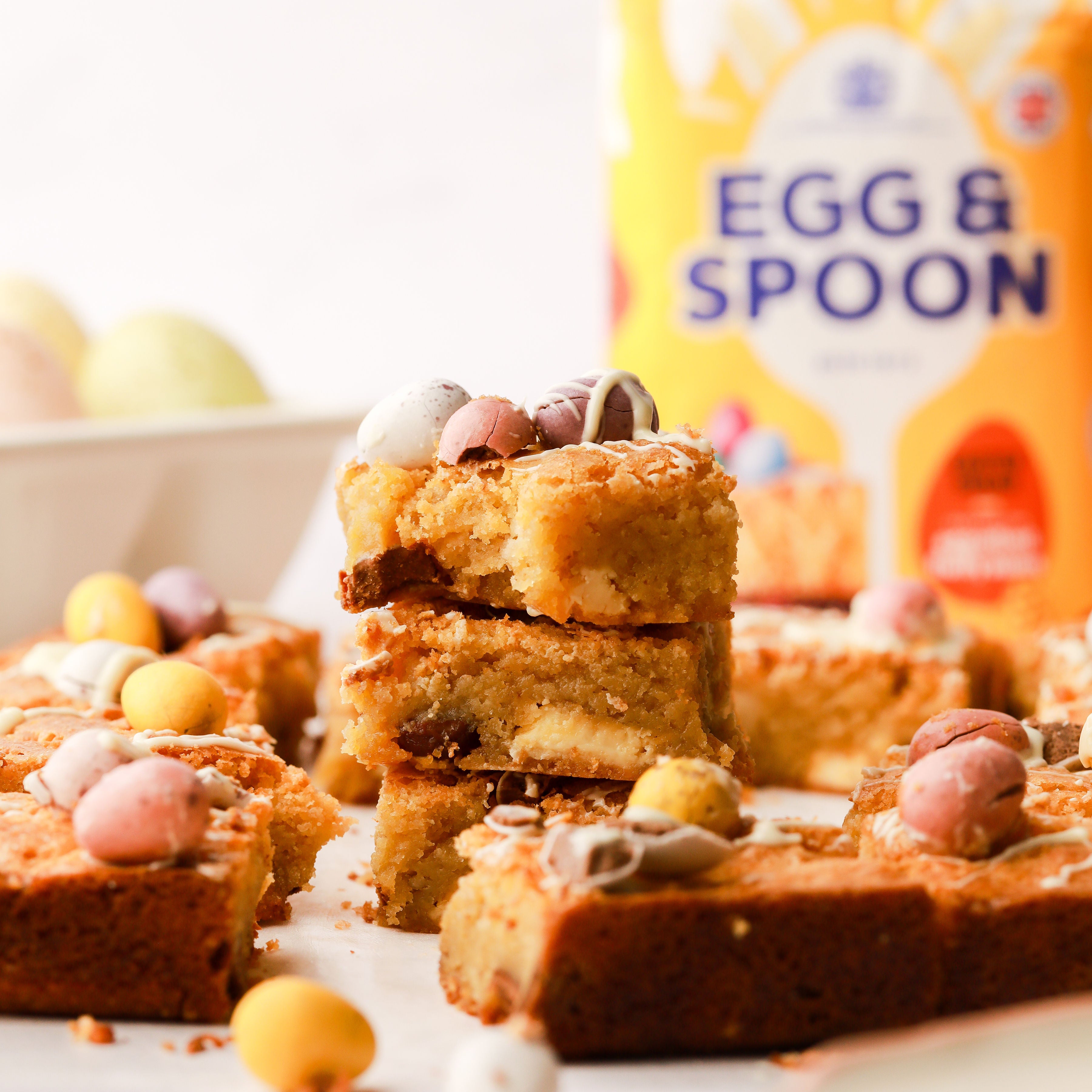Stacked slices of a freshly baked mini egg blondie that is decorated with mini chocolate eggs and white chocolate.